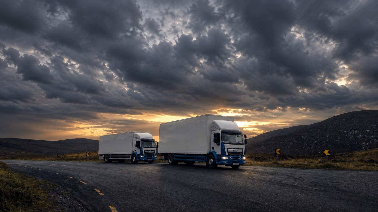 Two Esteeville box trucks on a mountain road at sunset